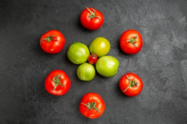 Top view red and green tomatoes around a cherry tomato on dark ground with copy space