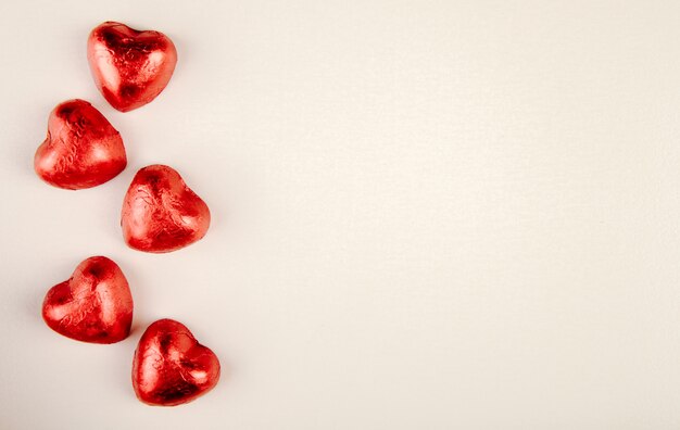 Вид сверху конфет в форме красного сердца, изолированных на белом столе с копией пространства