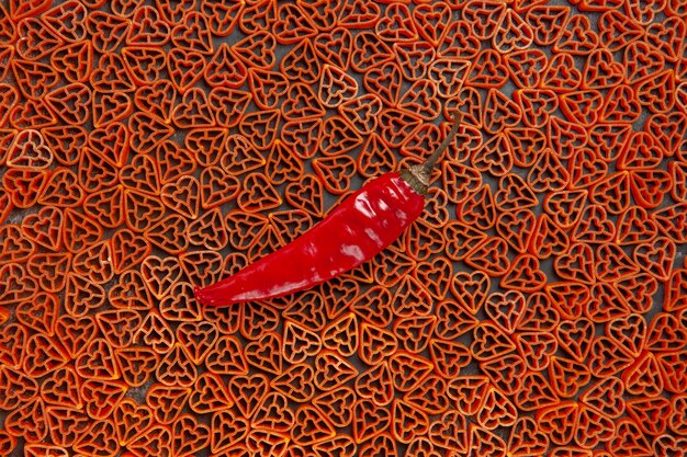 Foto gratuita vista dall'alto peperoncino rosso su pasta italiana a forma di cuore sul tavolo scuro