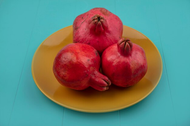 Top view of red juicy fresh pomegranates on a yellow plate on a blue background