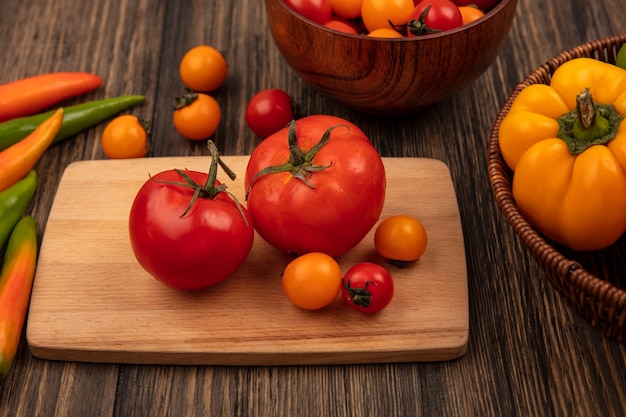 Вид сверху красных помидоров большого размера на деревянной кухонной доске с помидорами черри на деревянной миске и болгарским перцем на ведре на деревянной поверхности