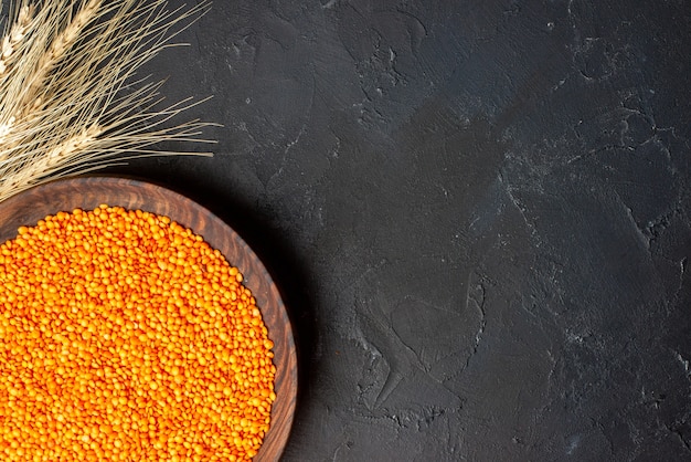 Top view of red lentils in a brown bowl spikes on the right side on black table