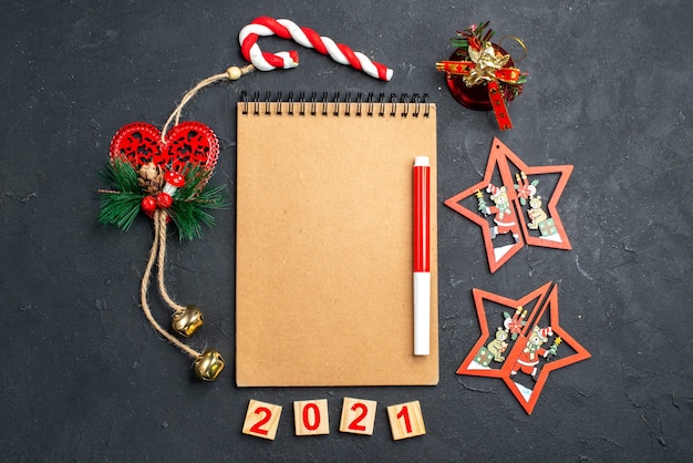 暗い孤立した表面の新年の写真のさまざまなクリスマスの飾りの円の中に立っているノートブックの上のビューの赤いマーカー