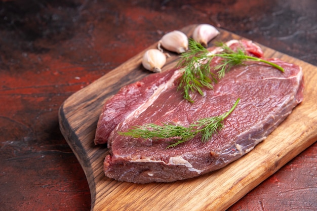 Вид сверху красного мяса на деревянной разделочной доске и зеленого чеснока на темном фоне