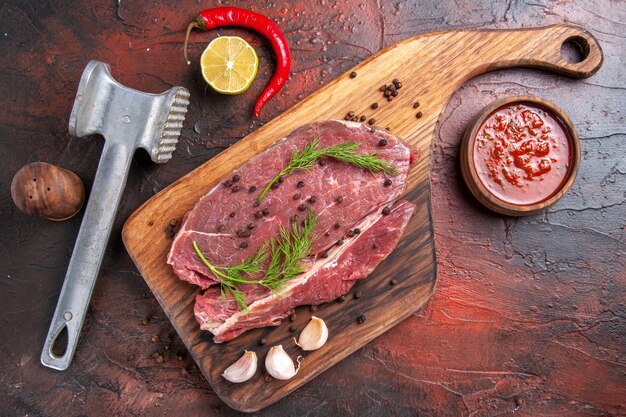 木製のまな板の赤身の肉と暗い背景映像のニンニク青唐辛子オイルボトルフォークとナイフの上面図