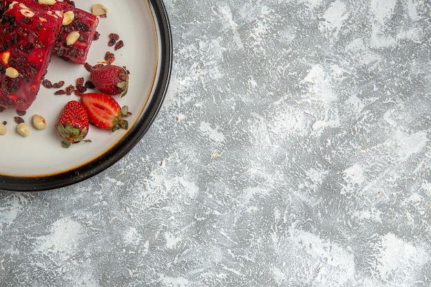 Top view red nougat sliced with nuts and fresh red strawberries on white surface