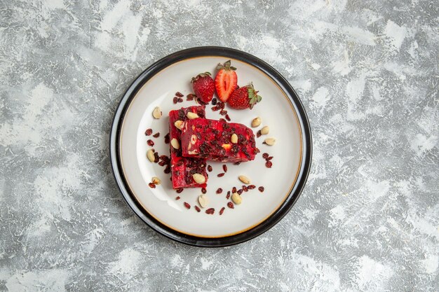 Top view red nougat sliced with nuts and fresh red strawberries on white surface