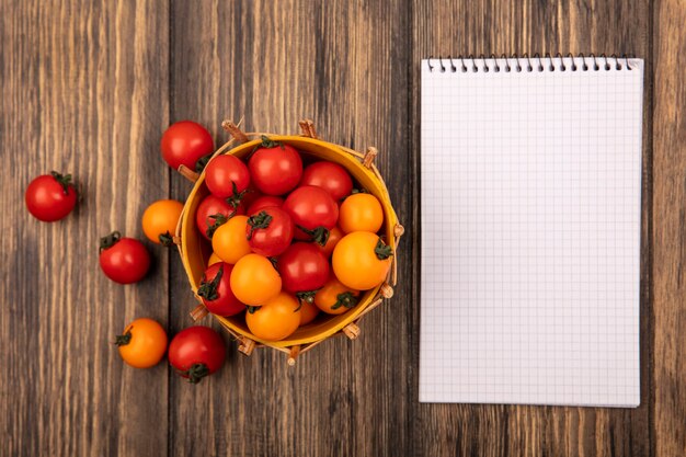 Top view of red and orange cherry tomatoes on a bucket with tomatoes isolated on a wooden wall with copy space