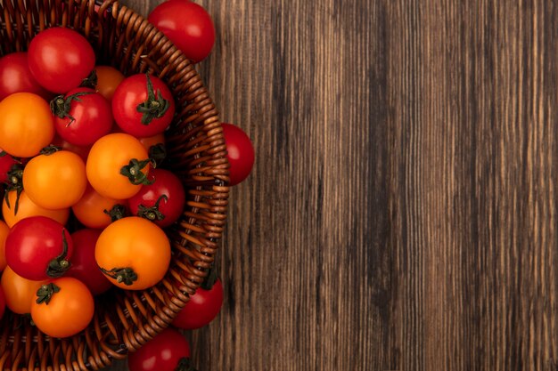 Top view of red and orange tomatoes on a bucket on a wooden wall with copy space