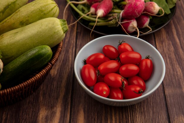 木製の表面のバケツにズッキーニキュウリなどの新鮮な野菜とボウルの上の赤い有機トマトの上面図