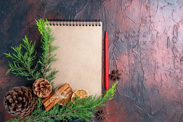 Top view red pen a notebook pine tree branches star anises pinecones dried lemon slices on dark red surface free place