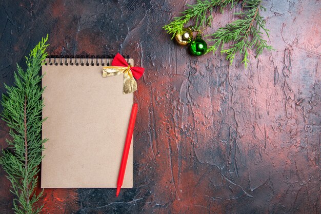 ノートブックの上面の赤いペン松の木の枝暗い赤の表面の空きスペースにクリスマスツリーのボール