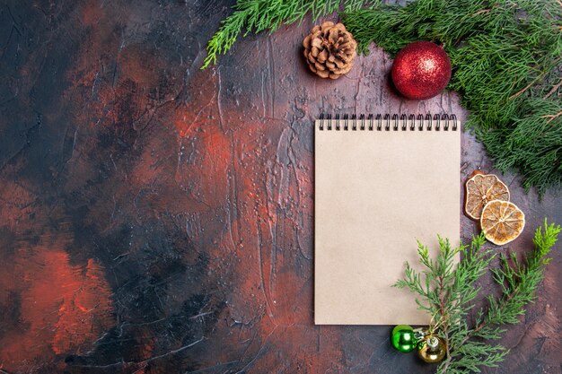 Top view red pen a notebook pine tree branches xmas tree ball toys dried lemon slices a cup of tea on dark red surface free space xmas photo