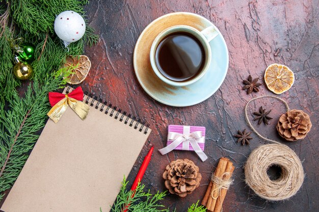 Top view red pen a notebook pine tree branches xmas tree ball toys straw thread star anises cup of tea on dark red surface copy space