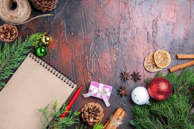 Top view red pen a notebook pine tree branches xmas tree balls and gift cinnamon anises straw thread dried lemon slices on dark red surface free space