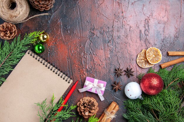 Top view red pen a notebook pine tree branches xmas tree balls and gift cinnamon anises straw thread dried lemon slices on dark red surface free space