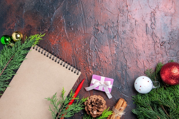 Top view red pen a notebook pine tree branches xmas tree toys and gift cinnamon anises straw thread on dark red table free place