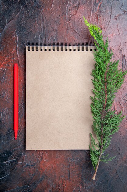 Top view red pen a notebook with small bow a pine tree branch on dark red surface with copy space