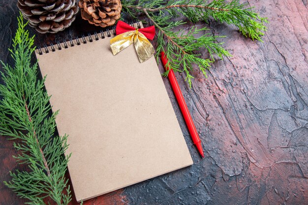 Top view red pen a notebook with small bow pine tree branches pinecones on dark red surface free space