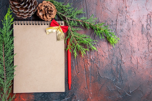 Top view red pen a notebook with small bow pine tree branches pinecones on dark red surface free space