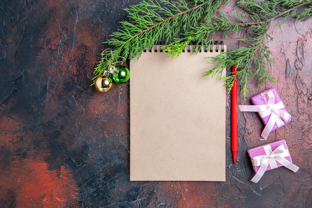 상위 뷰 빨간 펜 메모장 소나무 나무 가지 크리스마스 트리 장난감 및 어두운 빨간색 표면 여유 공간에 선물