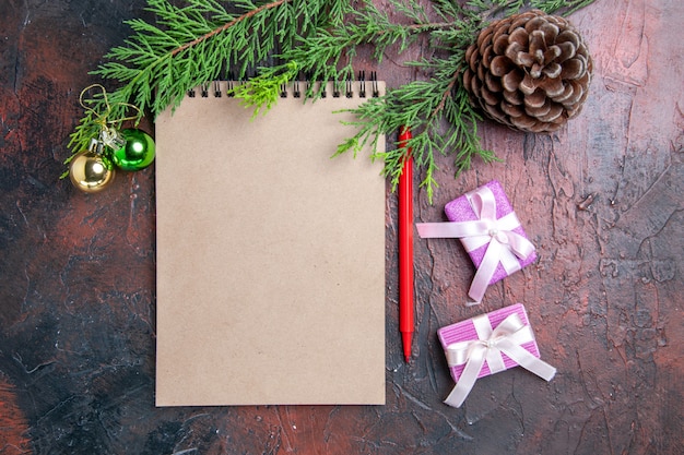 상위 뷰 빨간 펜 메모장 소나무 나무 가지 크리스마스 트리 장난감 및 선물 진한 빨간색 표면에 pinecone