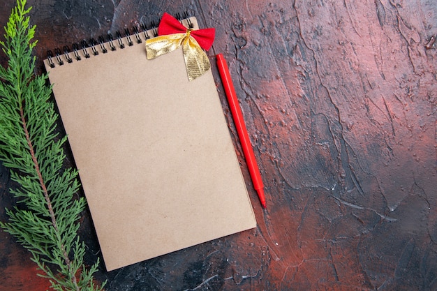 Free photo top view red pen a notepad with little bow a pine tree branch on dark red surface copy space