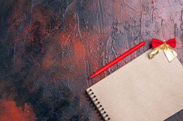コピースペースのある濃い赤の表面に小さな弓が付いたメモ帳の上面図の赤いペン