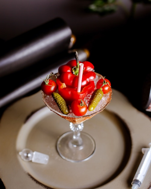 Top view of red pepper cocktail served in martini glass with cherry tomatoes and cornichons