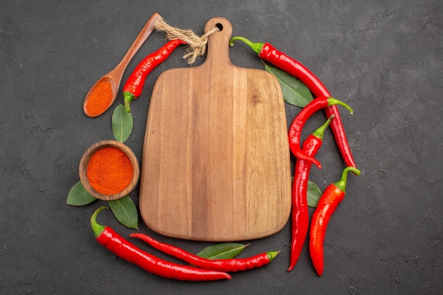 Top view red peppers a chopping board bay leaves a wooden spoon and a bowl of red pepper powder on the black table with copy space