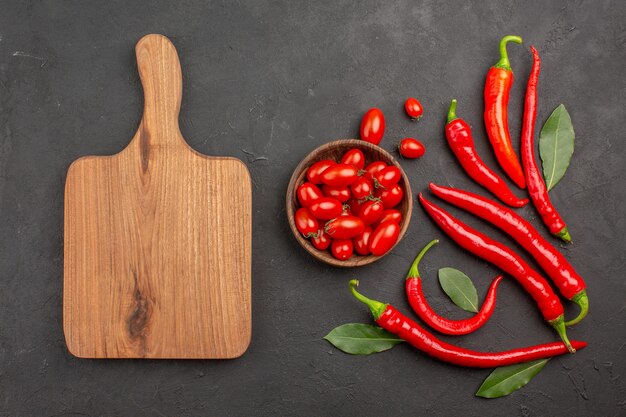 Top view red peppers and pay leaves and a bowl of cherry tomatoes and a chopping board on black table with copy space