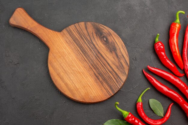 Top view red peppers and pay leaves and a chopping board on black table with copy space