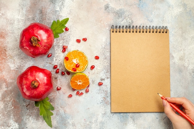 Free photo top view red pomegranates lemon slices red pencil in woman hand notebook on nude surface