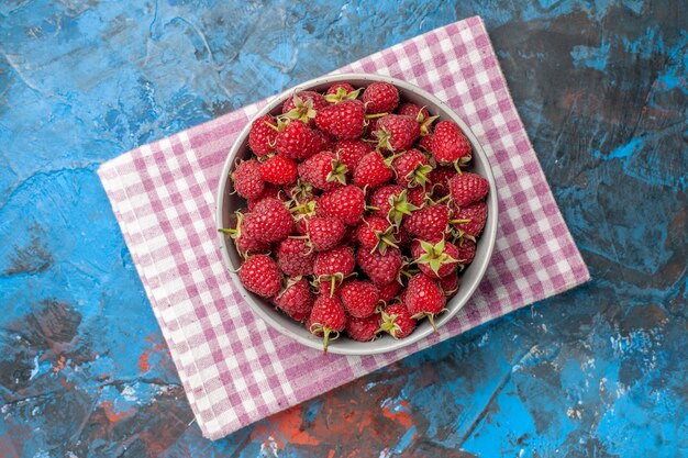 Top view red raspberries inside plate on blue background