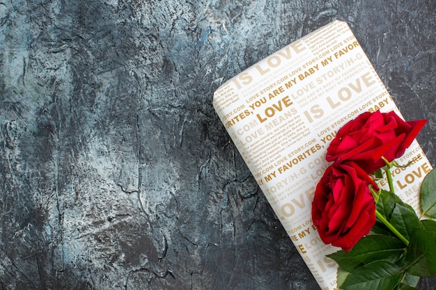 Top view of red roses on beautiful gift box on the left side on dark background