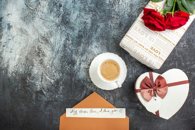 Вид сверху красных роз и красивых подарочных коробок, конверт с письмом чашка кофе для любимой на ледяном темном фоне
