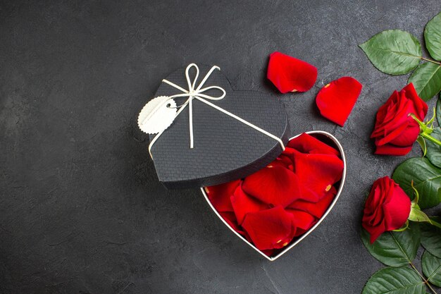 暗い背景のバレンタインデーのためのバラの花びらでいっぱいのボックスとトップビュー赤いバラは、カップルの色の情熱を感じている女性の心を愛しています