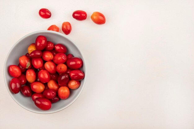 Top view of red sour cornelian cherries on a bowl on a white wall with copy space