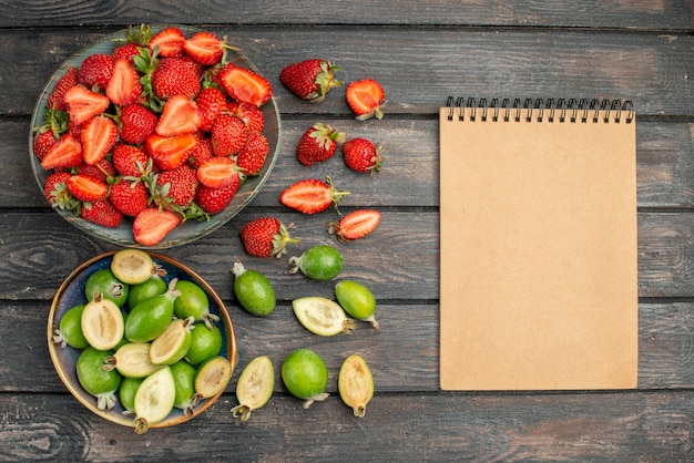 Top view red strawberries with fresh feijoas on dark wooden rustic desk