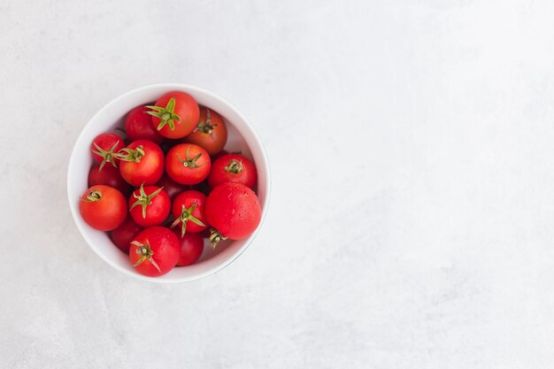 Top view of red tomatoes in the white bowl on white backdrop