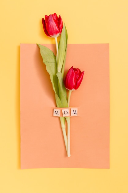 Top view of red tulip flowers with mother's day greeting card over yellow background