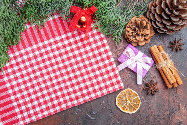 Top view red and white checkered tablecloth pinetree branches pinecones xmas gift cinnamon xmas tree ball toy on dark red background