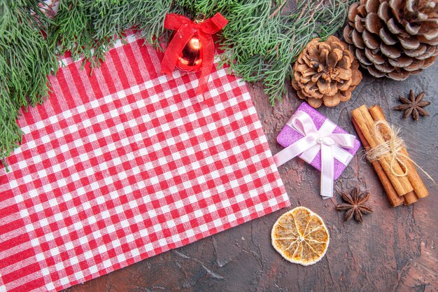 Top view red and white checkered tablecloth pinetree branches pinecones xmas gift cinnamon xmas tree ball toy on dark red surface