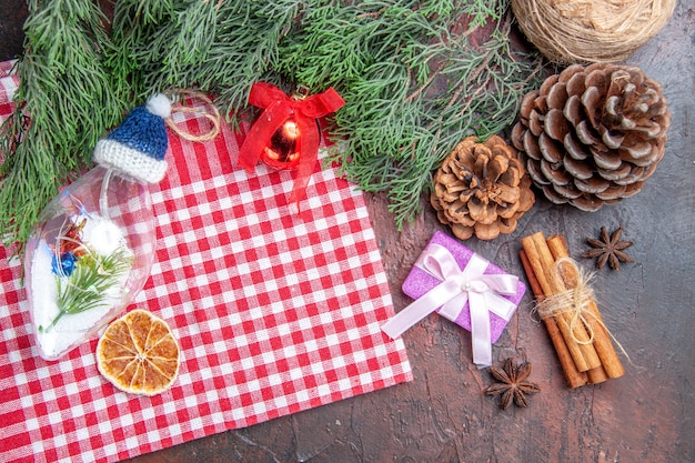 Top view red and white checkered tablecloth pinetree branches pinecones xmas gift cinnamon xmas tree toys star anises on dark red background