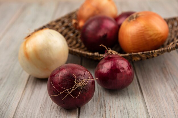 Top view of red and white onions on a wicker tray on a grey wooden surface