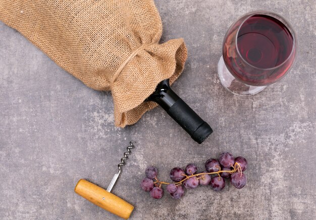 Top view red wine in sackcloth bag with glass and grape on dark stone  horizontal