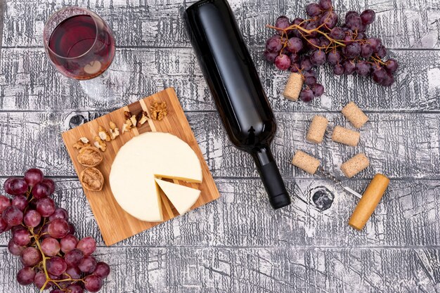 Вид сверху красное вино с виноградом и сыром на борту и на белой деревянной горизонтали