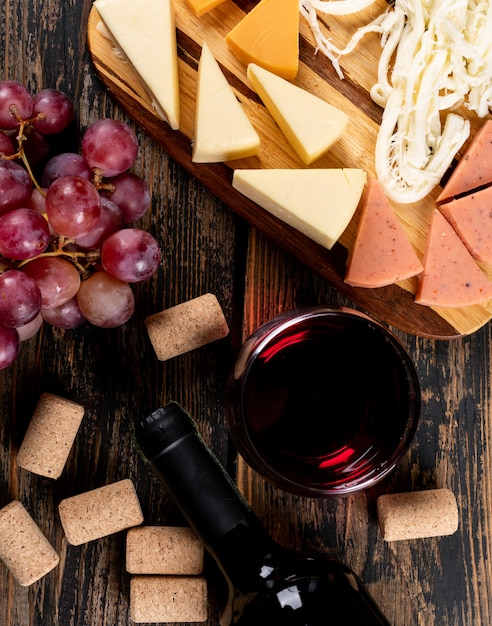 Top view of red wine with grape and cheese on cutting board on dark wooden  vertical