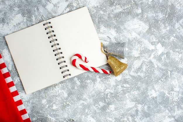 Foto gratuita vista dall'alto caramelle di natale rosse su taccuino campane di natale su spazio libero tavolo bianco grigio