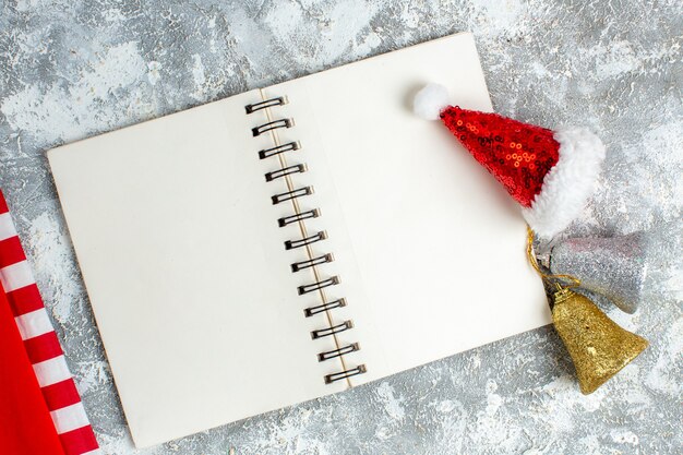 灰色の白いテーブルの上のノートブックのクリスマスの鐘の上面図赤いクリスマスのおもちゃ
